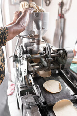 An adult tortilla maker is dropping some corn dough into the nixtamall mill in Mexico. Close up