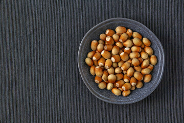 Shelled hazelnuts in a dark bowl on a black textile tablecloth