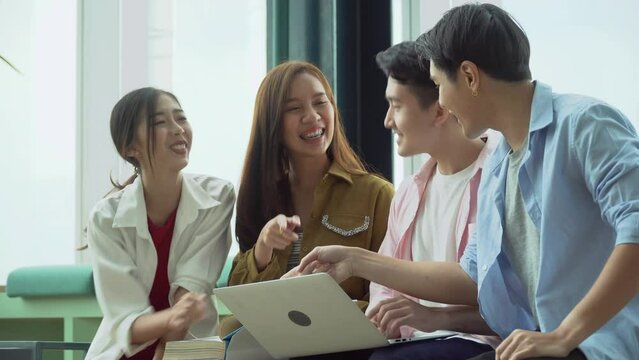 group of happy asian young university students brainstorming and discussion with laptop computer find information by internet and text book  in college library  science and technology subject . fun