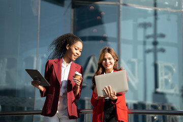 Two Asian businesswomen discussing business information while standing outside the office.