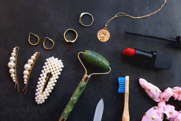 Various beauty products, accessories and jewelry on dark background. Top view.