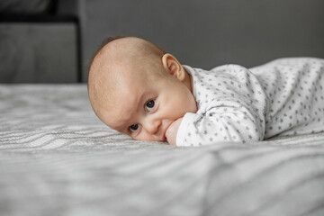 Child care concept. Portrait of cute little baby in bodysuit lying on blanket at home. Copy space