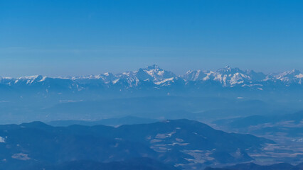 Panoramic view on summit cross of mountain peak Grosser Sauofen in winter on Saualpe, Lavanttal Alps, Carinthia, Austria, Europe. Snowcapped mountain ranges of Karawanks and Kamnik Savinja Alps