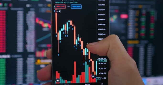 Trader investor holding smartphone analyzing financial crypto stock market price. Crypto investor using smartphone app for buying cryptocurrency in front of stock market financial screen, close up