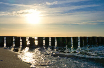 Groynes jut into the sea at sunset. The sun shines on the Baltic Sea. Landscape