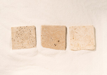 Three travertine tiles lying on a sand. Minimal composition with copy space. Top view.