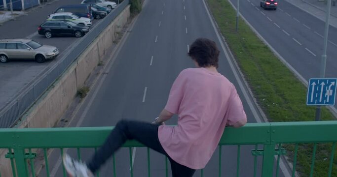 Climb over the railing guy's back, he stands on the bridge. He holds on to the support with his hands. The movement of cars on the road. Dangerous moment. CZ, Prague, Radlicka 30.9.22.