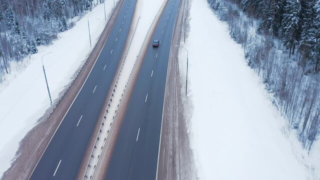A blue car drives along the road among a forest covered with snow and a truck. The car drives along the highway among snow-covered trees and roadsides in cold winter.