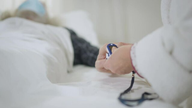 Unrecognizable woman measuring oxygen saturation level of ill man lying in bed with coronavirus. Caucasian senior wife taking care of husband putting on finger pulse oximeter in slow motion