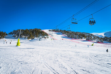 People riding up on a ski chair lift. People skiing and snowboarding down on the ski slope. Winter...
