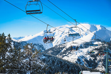 People riding up on a ski chair lift with snow capped mountains in the background. Winter holidays...