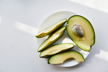 Green avocado fruit cut into slices on a white background. Avocado on a white plate. Avocado slices and halves