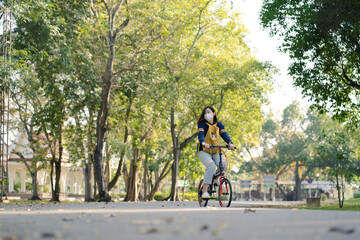 asian woman wearing facemask and biking bicycle with her cat in backpack at park