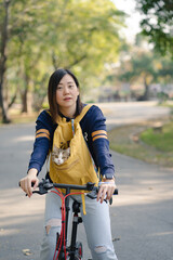 asian woman biking bicycle with her cat in backpack at park