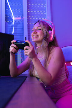 Cheerful female streamer in headphones using mic and gamepad