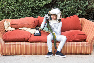 Boy in spacesuit having phone conversation on couch in park