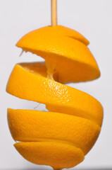 Fototapeta na wymiar orange cut in a spiral on a skewer on a white background