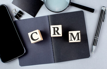 Word CRM on wooden block on black notebook with smartpone, credit card and magnifier