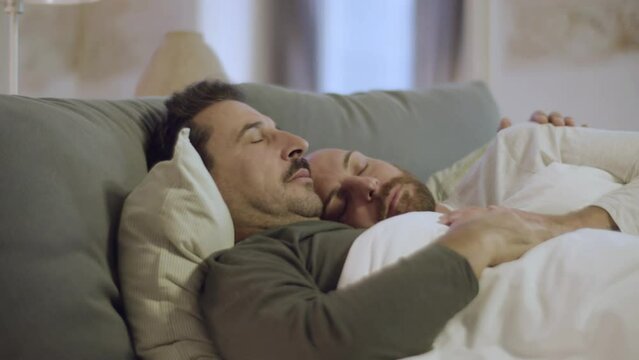 Handsome homosexual couple sleeping in bed and hugging. Close-up shot of peaceful bearded men in pajamas lying with closed eyes, resting together on weekend at home. Sleepy cycle, love, LGBT concept
