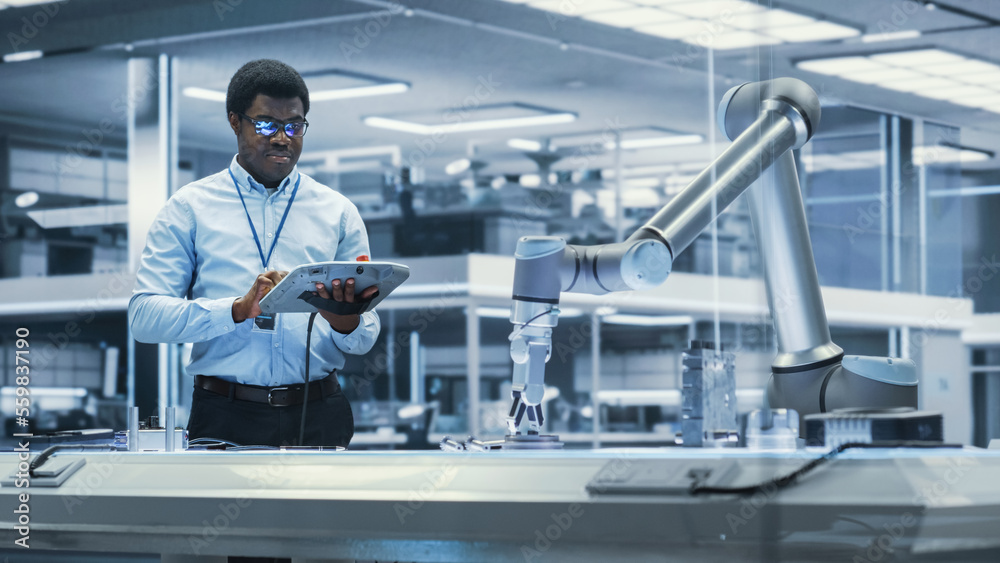 Aufkleber Young Black Male Engineer Using a Tablet Computer, Researching and Developing a Futuristic Robotic Arm Machine in a High Tech Industrial Laboratory with Modern Equipment.