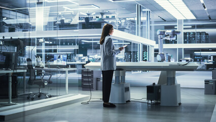 Young Female Engineer Using a Tablet Computer, Researching and Developing a Futuristic Robotic Arm Machine in a High Tech Industrial Laboratory with Modern Equipment.