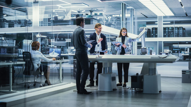 Professional Multicultural Team of Female and Male Engineers Using Industrial Programmable Robotic Arm in a Factory Development Workshop. Tech Facility with Machines, Computers and Research Equipment.