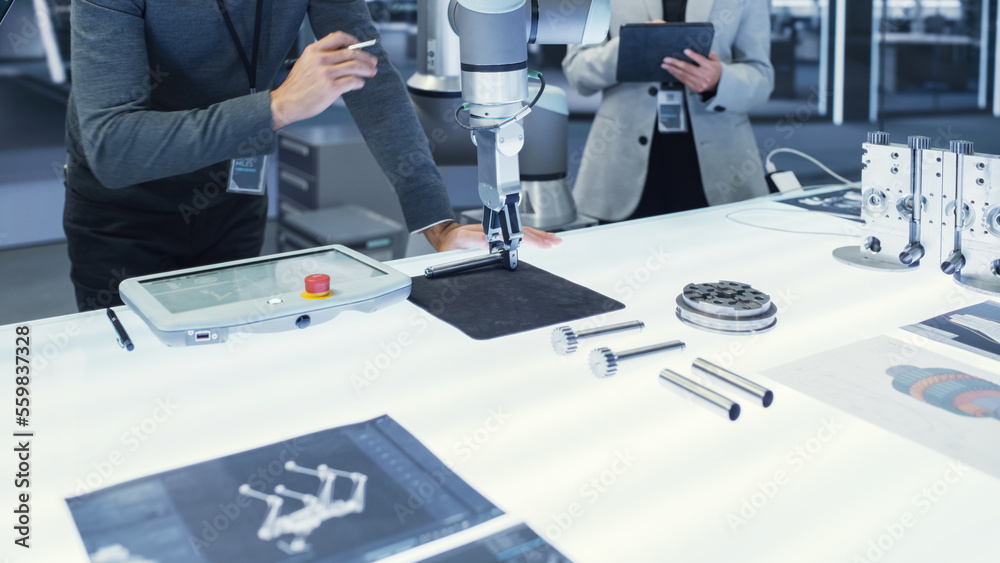 Fototapete Modern Robotic Arm Holding and Moving a Mechanical Metal Component. Diverse Team of Engineers Using Tablet Computer to Manipulate and Program the Robot.