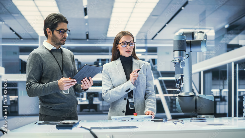 Fototapete Robotics Engineer and Machinery Operator Collaborate on a Robot Arm Project at a Factory, Using a Tablet Computer to Operate the Robot Arm in Scientific Technology Lab.