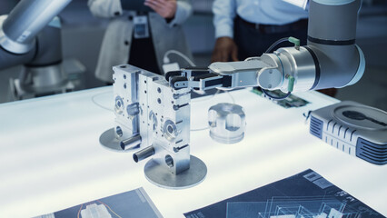 Close Up Shot of a Modern Robotic Arm Picking Up and Moving a Mechanical Metal Component. Group of Engineers Using Tablet Computer to Manipulate and Program the Robot.