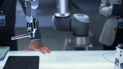 Close Up Shot of a Modern Robotic Arm Holding and Moving a Mechanical Metal Component. Diverse Team of Engineers Using Tablet Computer to Manipulate and Program the Robot.