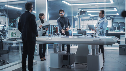 Diverse Team of Industrial Robotics Engineers Gathered Around a Table With Robotic Arm. Scientists...