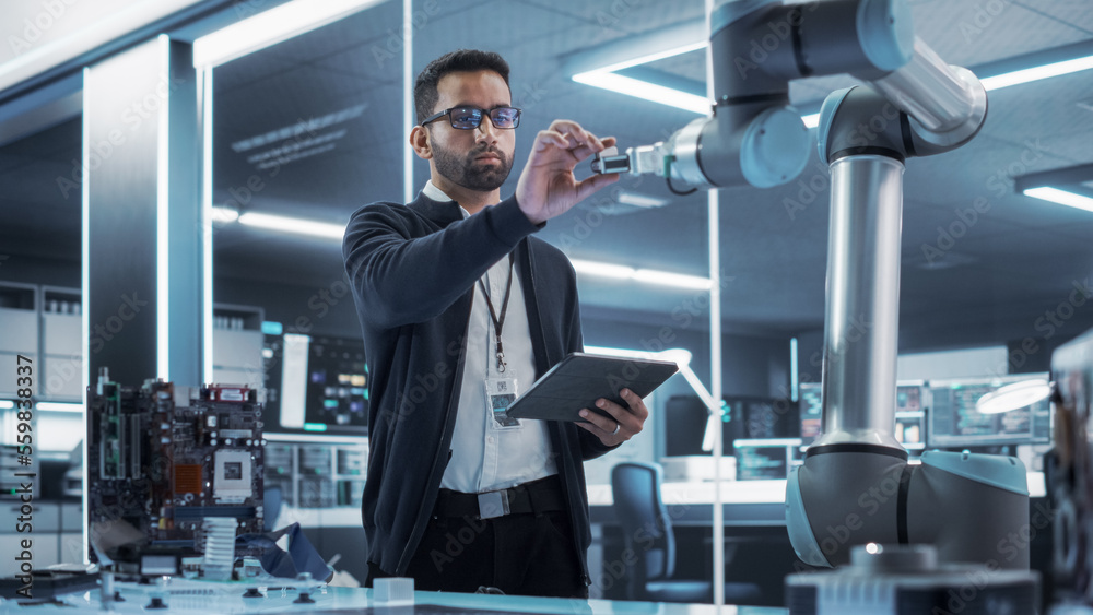 Poster Portrait of a Young Multiethnic Male Engineer Using Tablet Computer. Interacting with a Robotic Arm Machine, Receiving a Microchip from the Hand. High Tech Industrial Laboratory Facility.