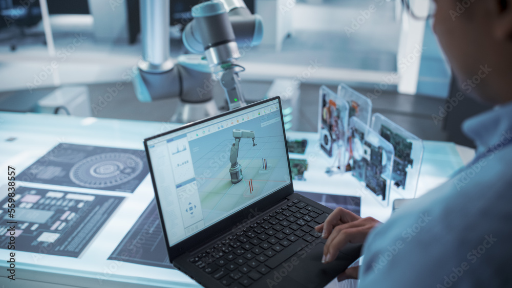Poster Over the Shoulder Shot of a Robotics Engineer Using a Laptop Computer with a Software Operating the Robotic Arm. Robot Hand Holding a Microchip. Automation Startup Research and Development Office.