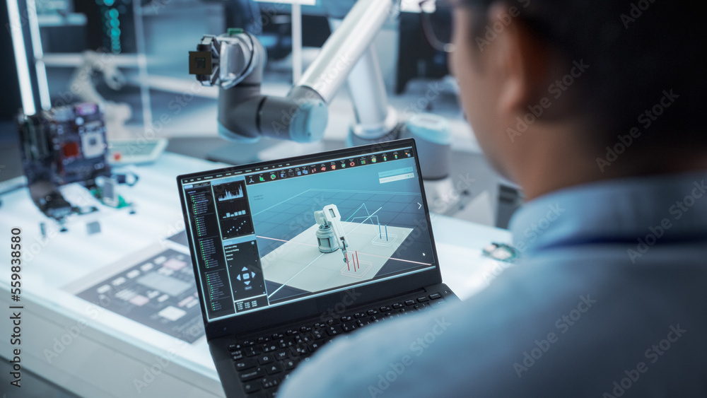 Poster Over the Shoulder Shot of a Robotics Engineer Using a Laptop Computer with a Software Operating the Robotic Arm. Robot Hand Holding a Microchip. Automation Startup Research and Development Office.