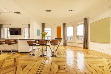 Large living room with many windows facing the street with gray curtains, beautiful laminated floors of varnished hardwoods and an island with high stools in the middle