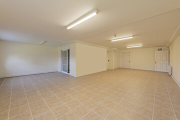 Empty living room of a ground floor residential townhouse with tiled floors, French style windows and white wooden and fire doors and long ceiling lamps