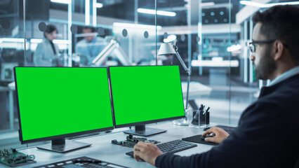 Software Developer Working on a Desktop Computer with Two Green Screen Chromakey Display Screens in...