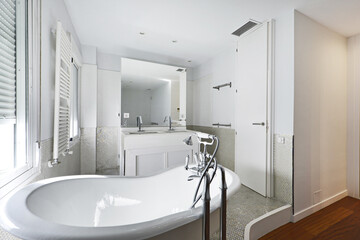 Bathroom with claw-foot bathtub, white wooden furniture with built-in mirror and white radiator towel rail and tiled tiles