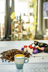 A small blue porcelain espresso cup on a table full of coffee beans and pods near the window