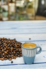 A small blue porcelain espresso cup on a blue planked table top filled with coffee beans