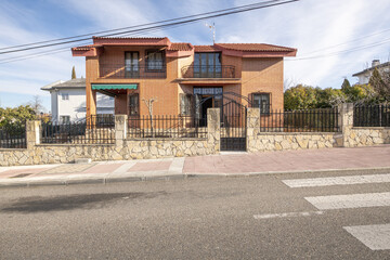 Fototapeta na wymiar Detached house with a plot with a stone and metal perimeter fence seen from the other side of the street