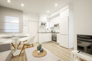 Studio apartment with an open plan kitchen with white cabinets and a round white dining table with...