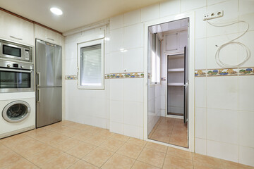 Empty one-story kitchen except for the kitchen furniture with access to a pantry with white aluminum and glass doors