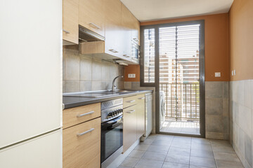 Kitchen furnished with light wood furniture with a gray countertop and a brown anodized aluminum door that opens onto a drying terrace with a washing machine