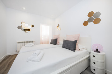 Bedroom with a white wooden headboard, gray and pink cushions, a white wooden bed, circular bedside...