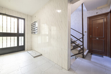 Portal of an old residential building with metal stairs and stone steps and similar marble tiling and sapele wood doors