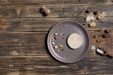 A plate with French foie gras served with nuts, pepper, salt, and dried fruits on the wooden table, top view with copy space © t.sableaux