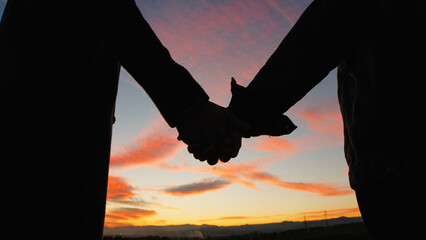 hand by hand in silhouette for a couple against sunset sky