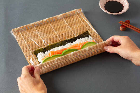Crop person rolling sushi with bamboo mat