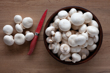 Fresh champignons on the table, in a bowl and on a wooden board with a red knife, top view of vegetable ingredients for cooking